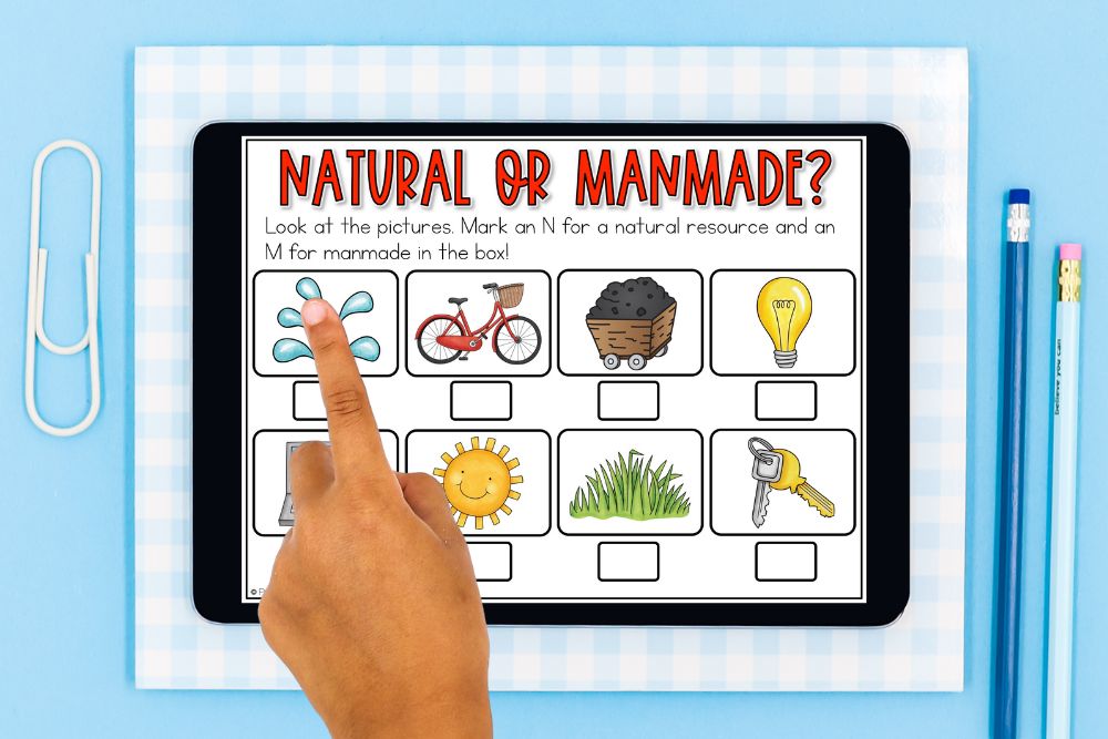 Natural Resources Lesson Plans Kids Will Love A child's hand pointing to a natural resources sorting activity on a tablet, showing pictures of water, a bicycle, coal, a lightbulb, a computer, the sun, grass, and keys on a blue gingham background with pencils.